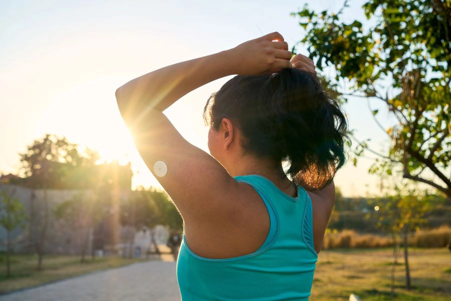 638979555639426875Young Latin sportswoman tying hair with glucose sensor or monitor at sunset in park